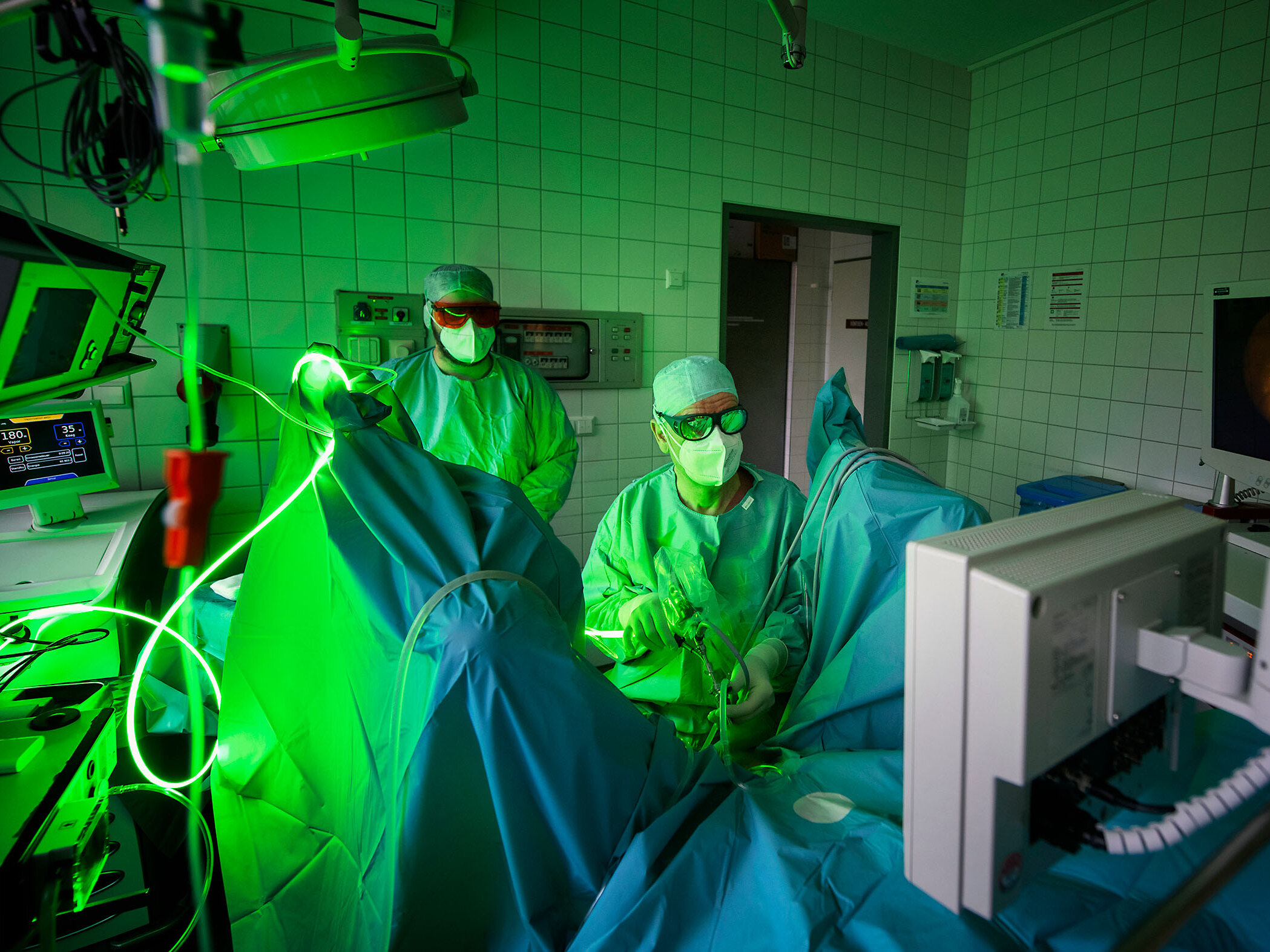 Urologen in grünem Licht führen einen Eingriff durch und konzentrieren sich dabei auf einen Monitor, der ein Bild im Operationssaal anzeigt.