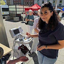 Eine junge Frau mit dunklen Haaren steht neben einem medizinischen Gerät. 