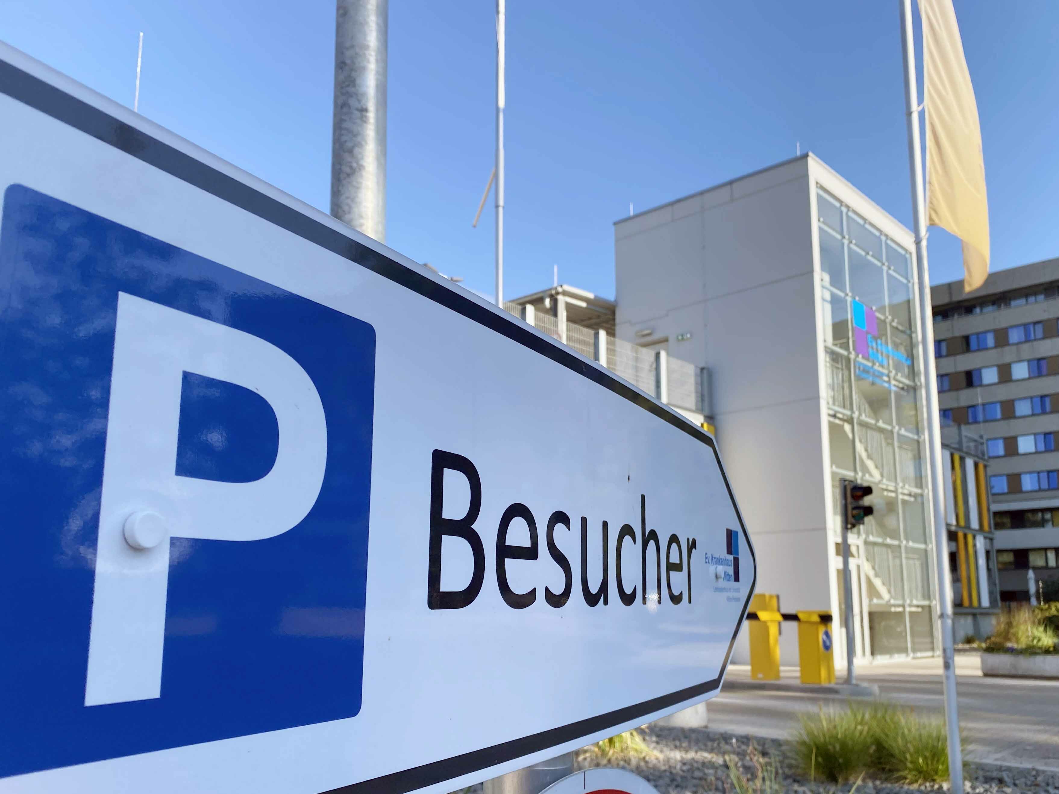 Nahaufnahme eines "Besucher"-Parkplatzschilds in der Nähe eines modernen Gebäudes unter strahlend blauem Himmel.