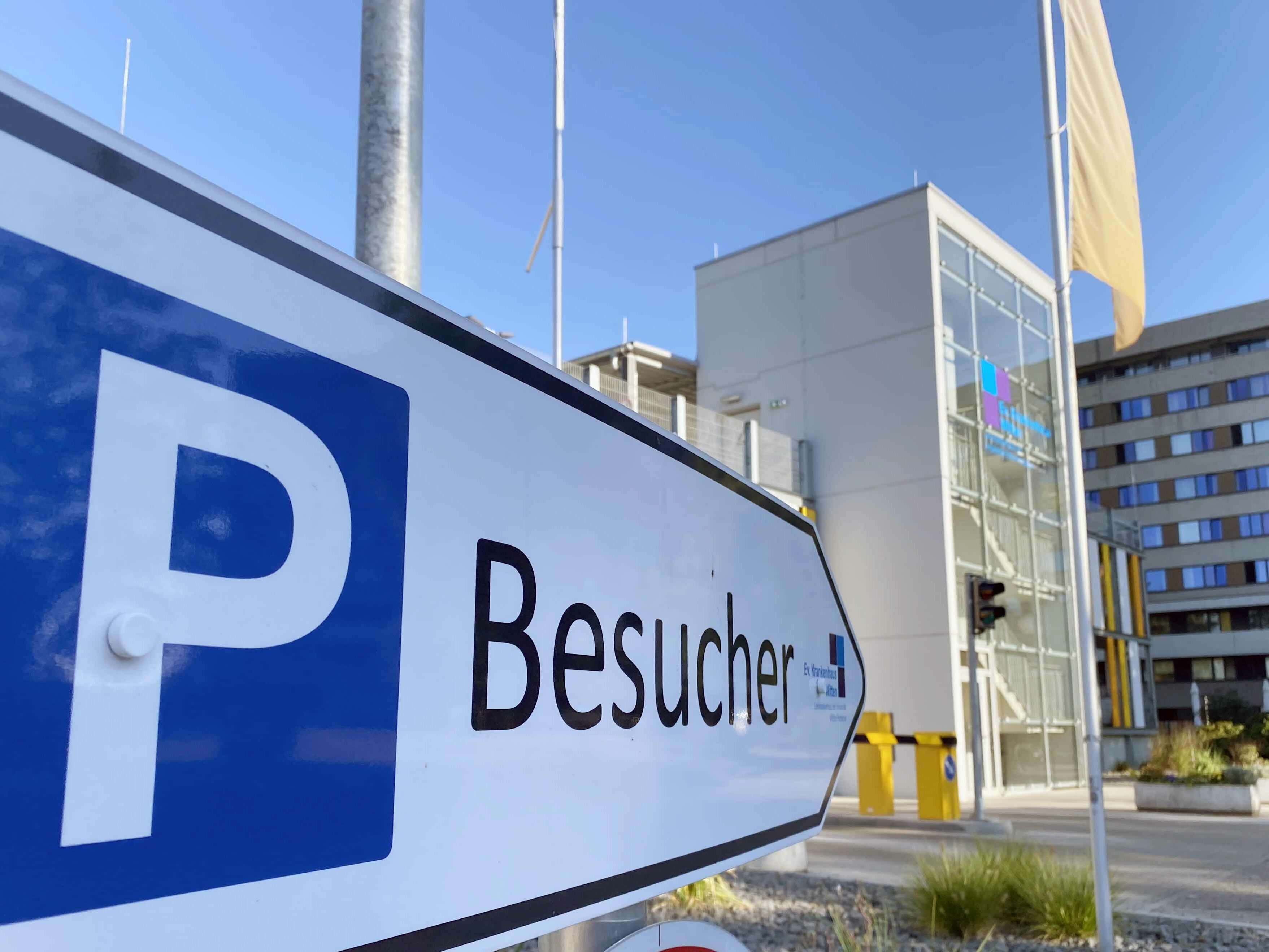 Nahaufnahme eines "Besucher"-Parkplatzschilds in der Nähe eines modernen Gebäudes unter strahlend blauem Himmel.