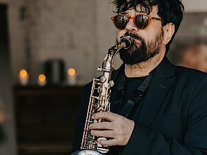 Schwarz gekleiderter Mann mit Sonnenbrille spielt auf dem Saxophon.