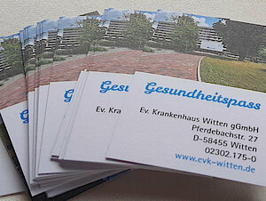 Ein Stapel "Gesundheitspass"-Karten der Ev. Krankenhaus Witten gGmbH, mit Kontaktdaten und einem Gebäudefoto.