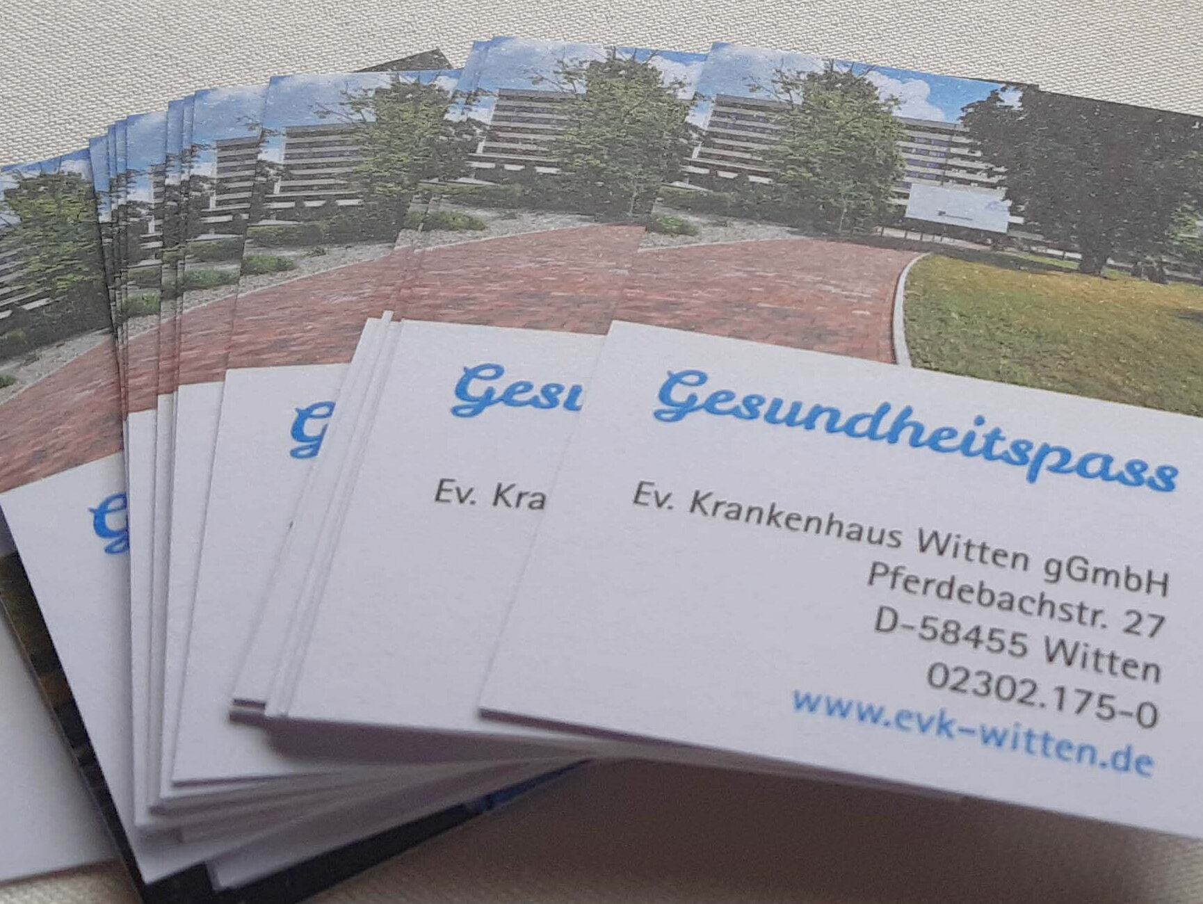 Ein Stapel "Gesundheitspass"-Karten der Ev. Krankenhaus Witten gGmbH, mit Kontaktdaten und einem Gebäudefoto.