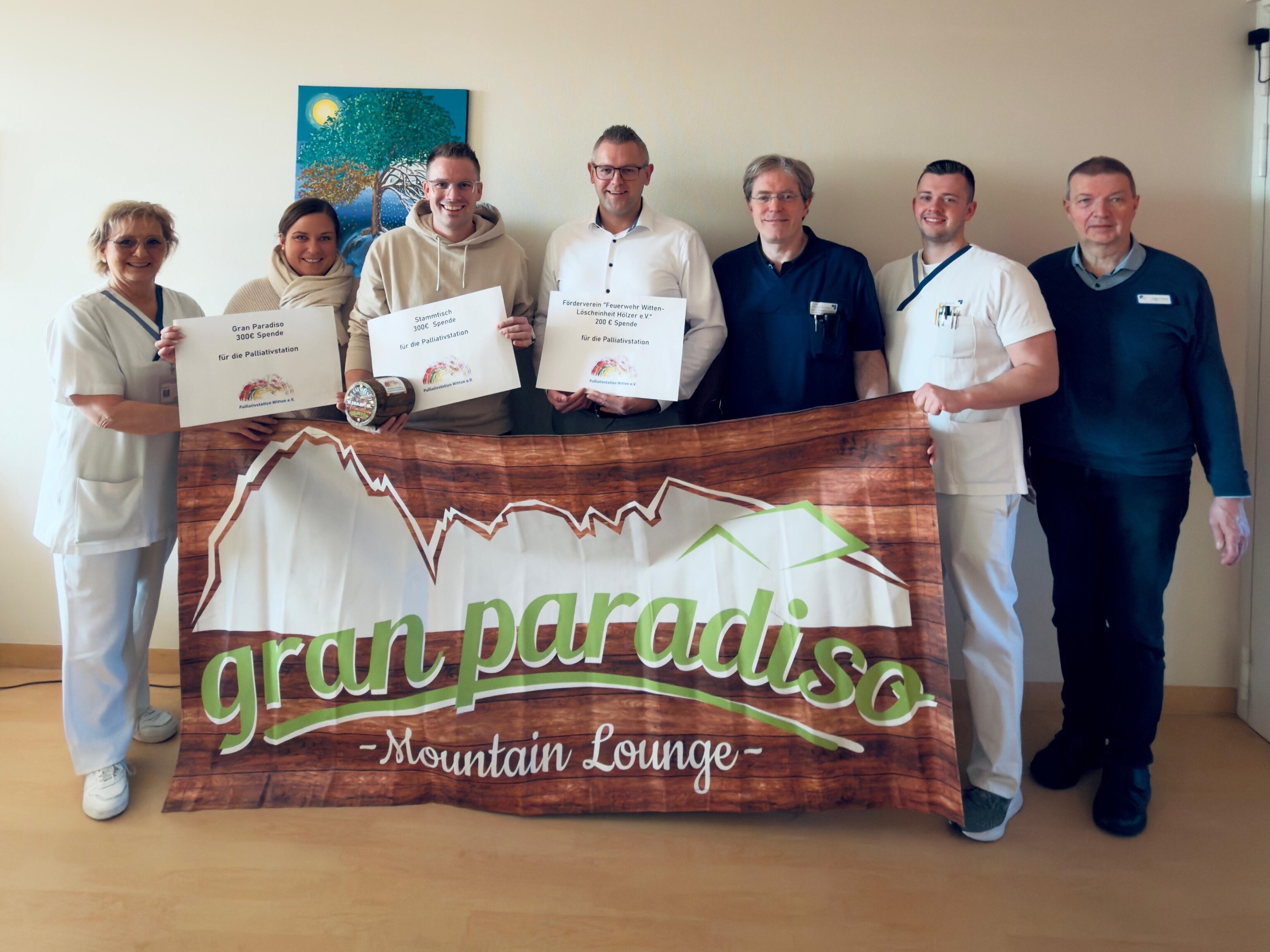 Männer und Frauen, einige von ihnen in weißen und dunkelblauen Kassaks, andere in normaler Kleidung, stehen vor einer Wand und halten Zettel sowie ein Banner mit der Aufschrift "gran paradiso" in der Hand.
