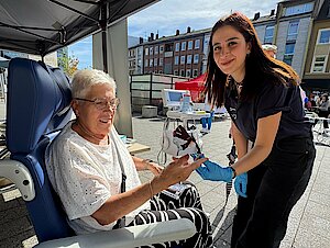 Eine ältere Frau sitzt in einem Rollstuhl. Eine dunkelhaarige jüngere Frau misst den Blutzucker. 