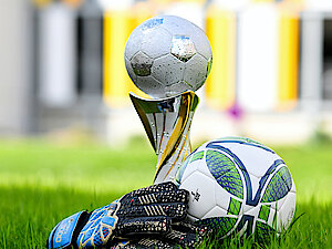Auf einer Wiese liegen ein Fußball, Handschuhe und ein Pokal. 