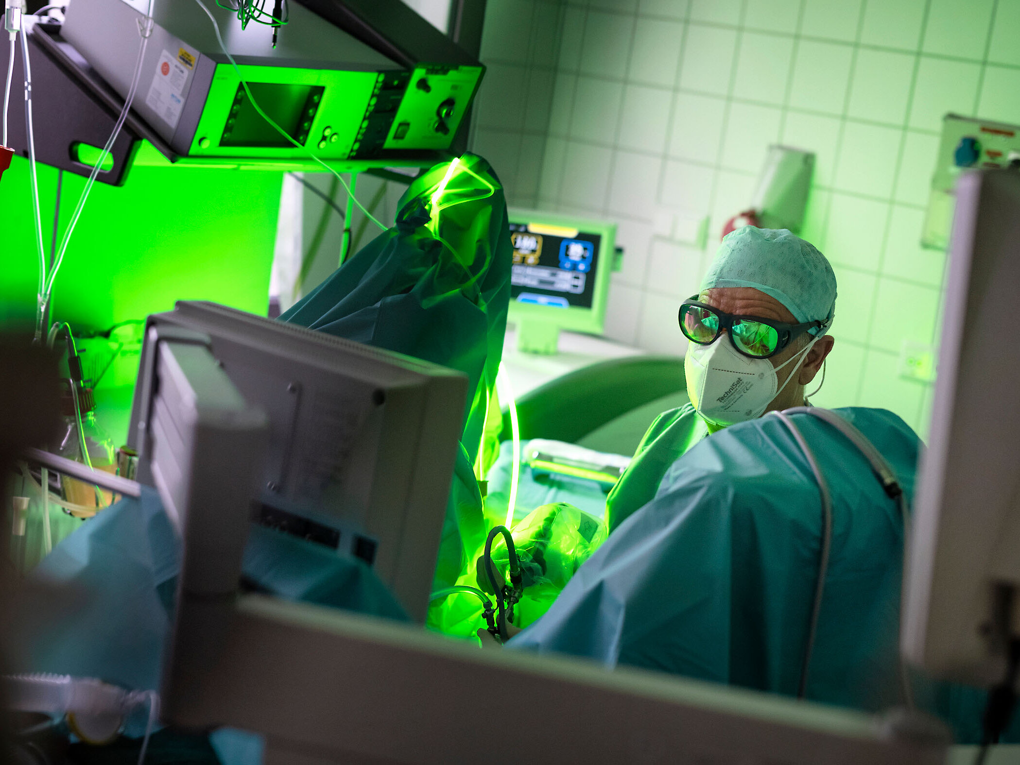 Urologe mit Maske und Kittel operiert in einem hell erleuchteten Krankenhauszimmer mit einem grünen Lasergerät.