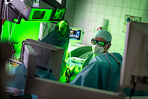 Urologe mit Maske und Kittel operiert in einem hell erleuchteten Krankenhauszimmer mit einem grünen Lasergerät.