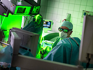 Urologe mit Maske und Kittel operiert in einem hell erleuchteten Krankenhauszimmer mit einem grünen Lasergerät.