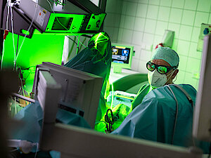 Urologe mit Maske und Kittel operiert in einem hell erleuchteten Krankenhauszimmer mit einem grünen Lasergerät.