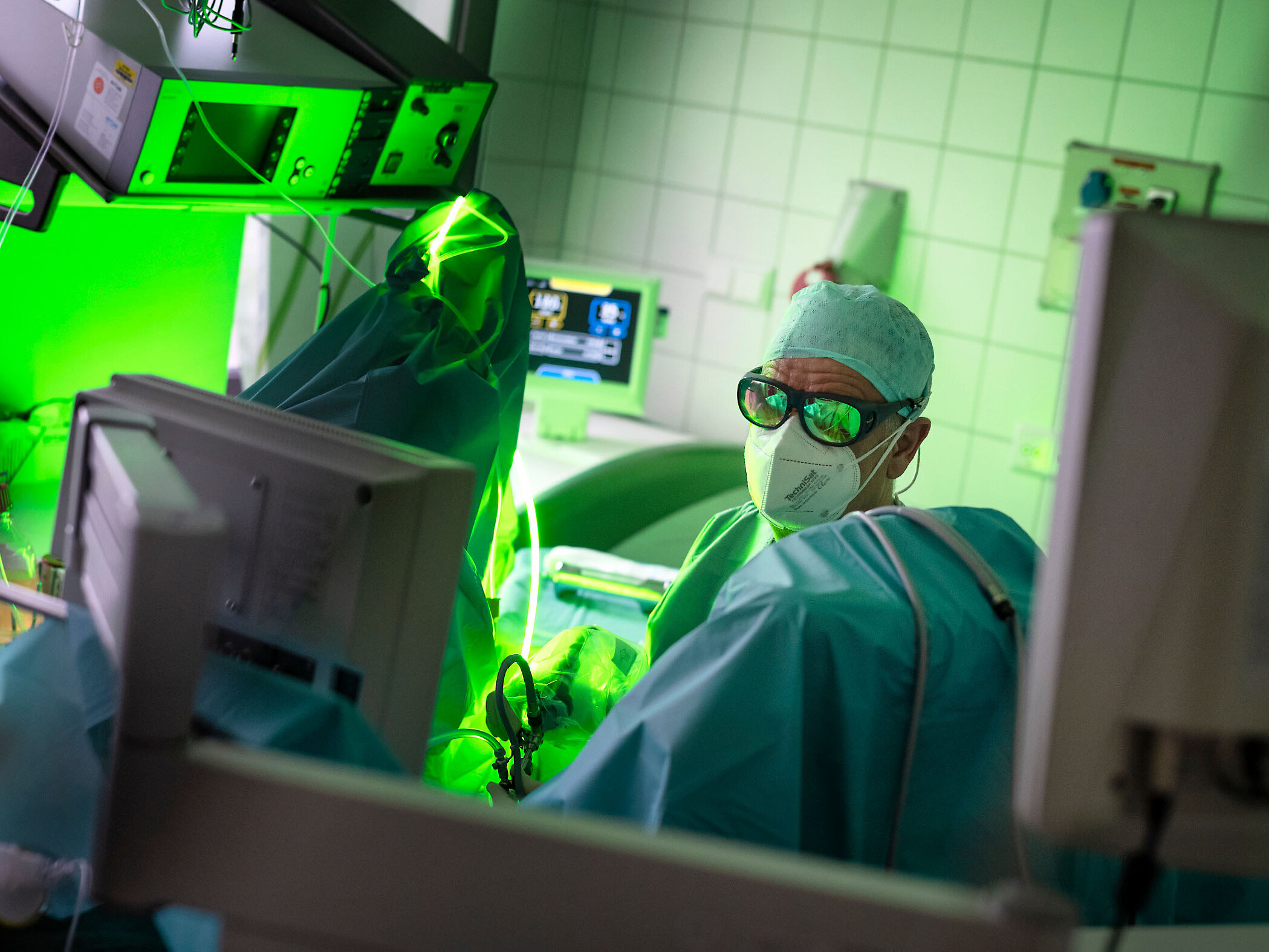 Urologe mit Maske und Kittel operiert in einem hell erleuchteten Krankenhauszimmer mit einem grünen Lasergerät.