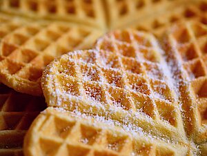 Nahaufnahme von herzförmigen Waffeln, die mit Puderzucker bestreut sind.