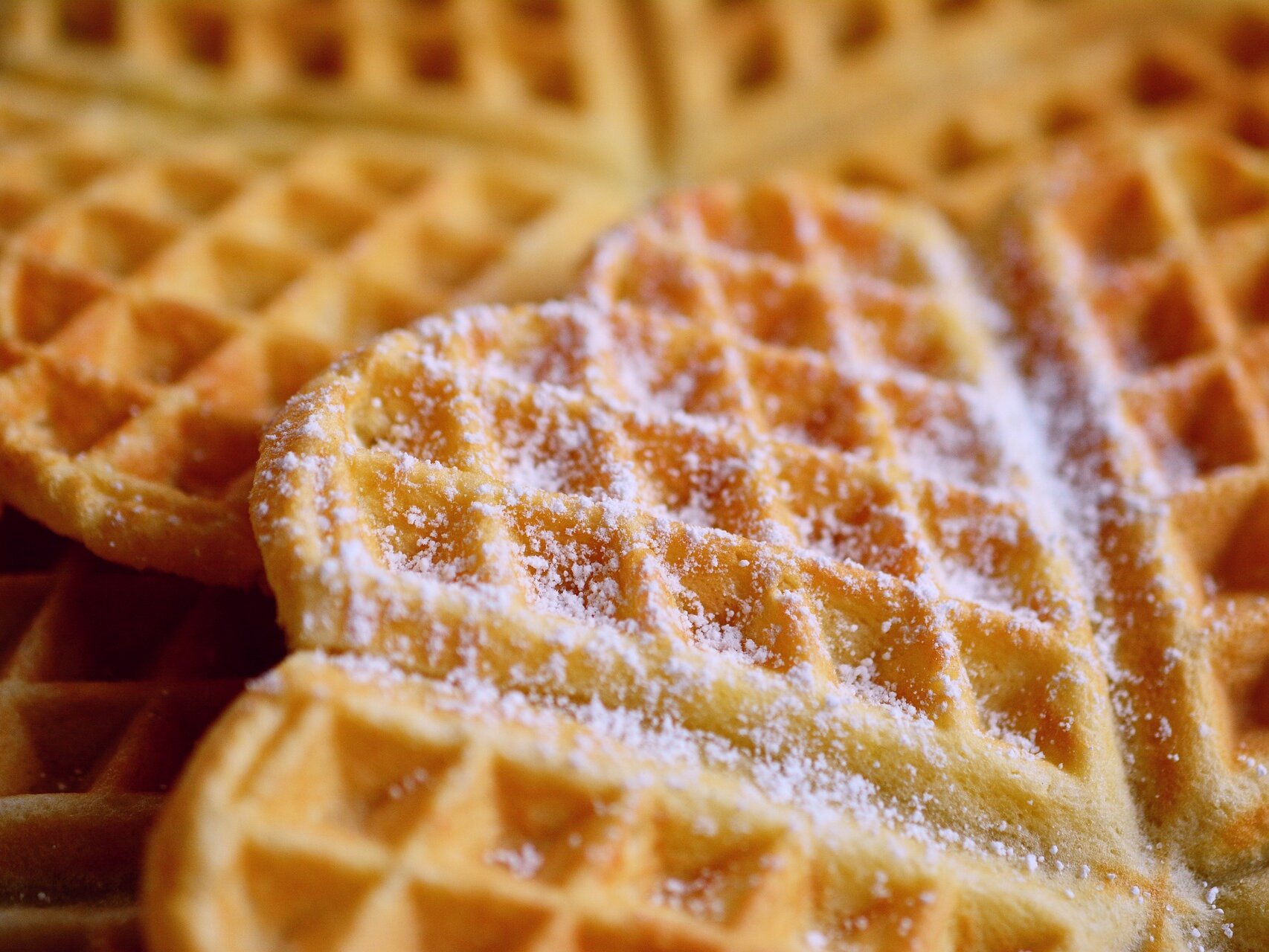 Nahaufnahme von herzförmigen Waffeln, die mit Puderzucker bestreut sind.